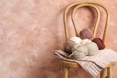 Photo of Different yarns, crochet hook and project on chair near beige wall. Space for text