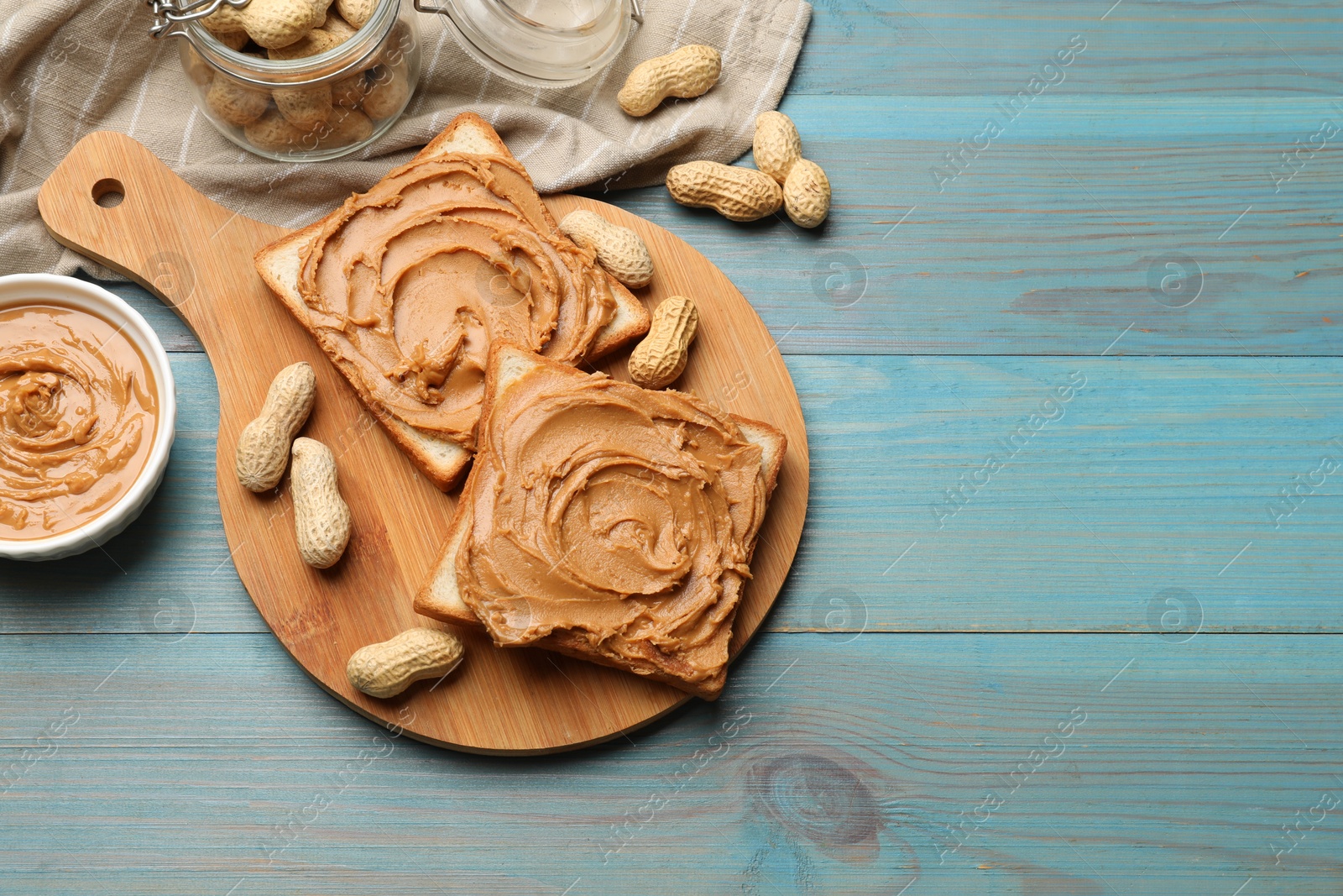 Photo of Tasty sandwiches with peanut butter and nuts on light blue wooden table, flat lay. Space for text