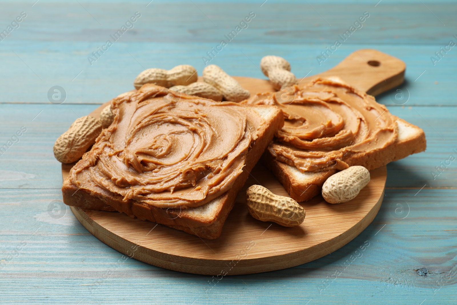 Photo of Tasty sandwiches with peanut butter and nuts on light blue wooden table, closeup