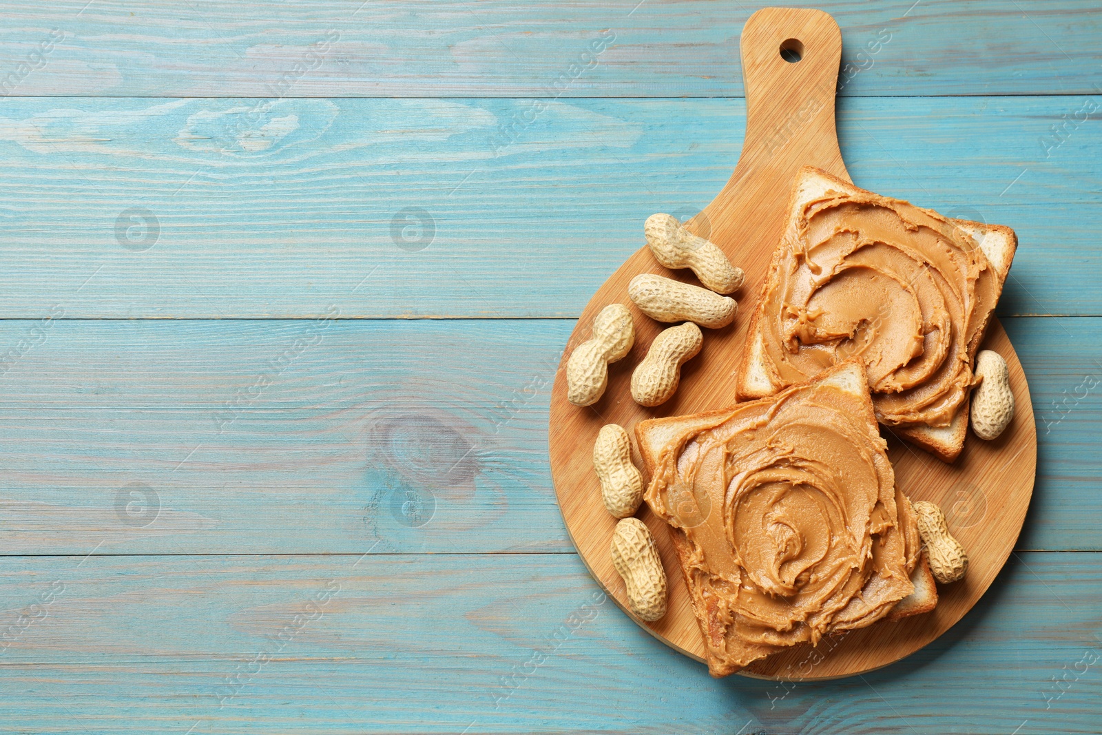 Photo of Tasty sandwiches with peanut butter and nuts on light blue wooden table, top view. Space for text