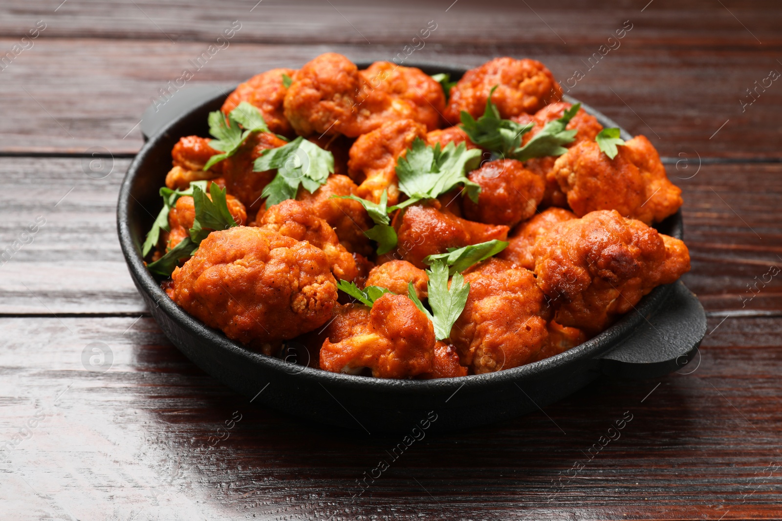 Photo of Baked cauliflower buffalo wings with parsley in baking dish on wooden table, closeup