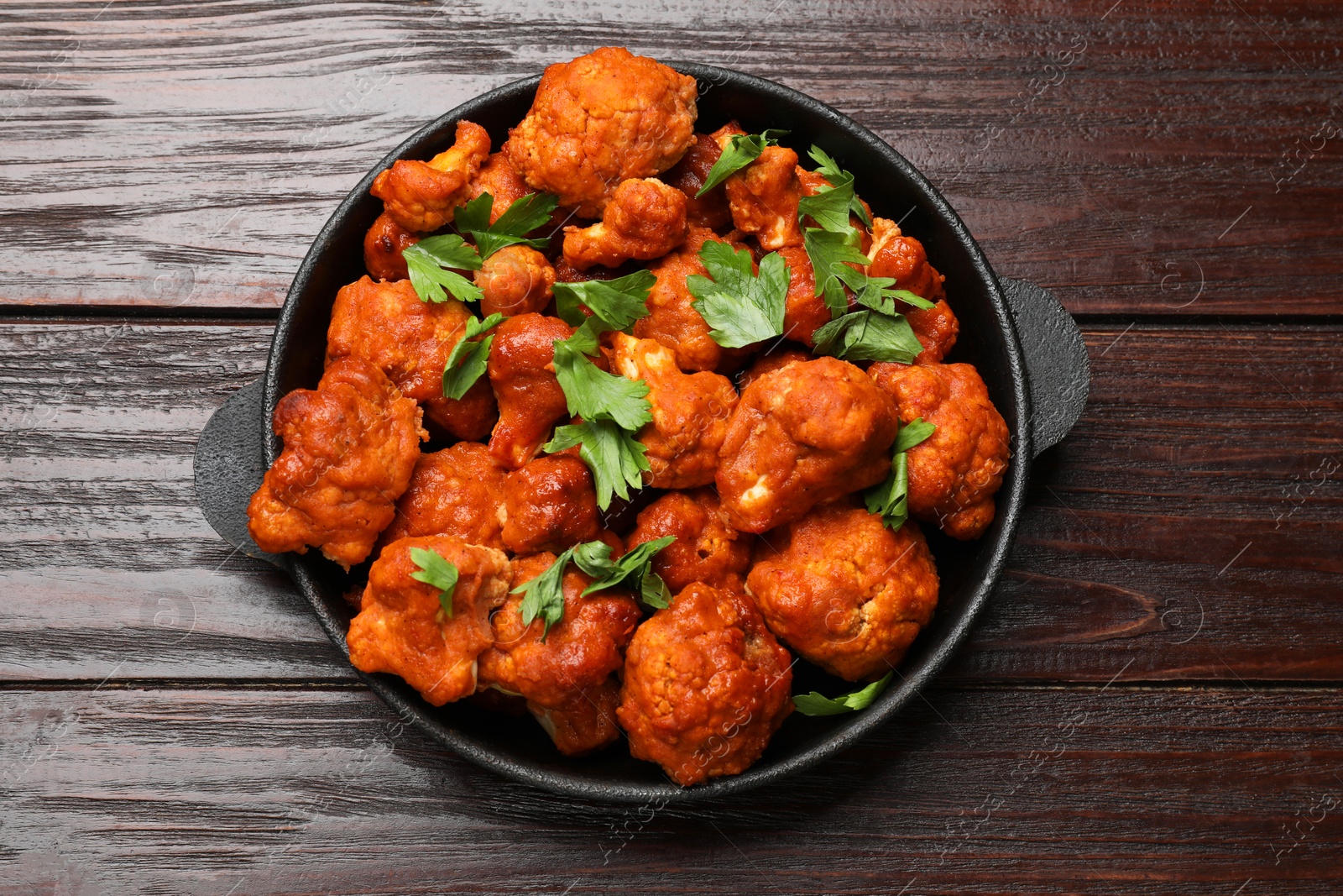 Photo of Baked cauliflower buffalo wings with parsley in baking dish on wooden table, top view