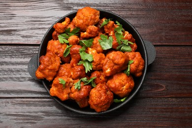 Photo of Baked cauliflower buffalo wings with parsley in baking dish on wooden table, top view