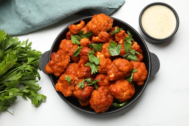 Photo of Baked cauliflower buffalo wings in baking dish, parsley and sauce on white table, top view