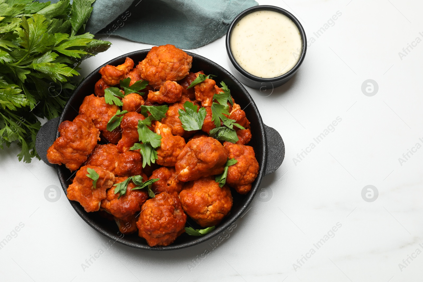 Photo of Baked cauliflower buffalo wings in baking dish, parsley and sauce on white marble table, top view. Space for text