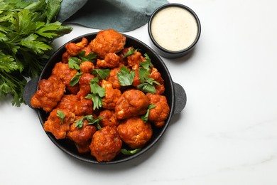 Photo of Baked cauliflower buffalo wings in baking dish, parsley and sauce on white marble table, top view. Space for text