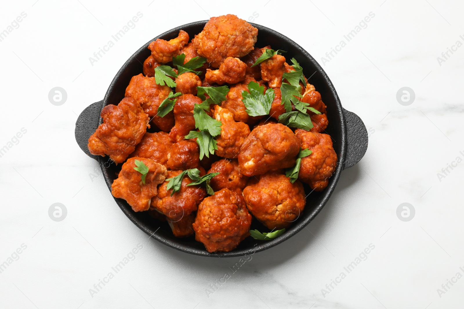 Photo of Baked cauliflower buffalo wings with parsley in baking dish on white marble table, top view