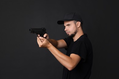 Young bodyguard using gun on black background