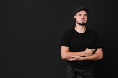 Young bodyguard with gun on black background, space for text