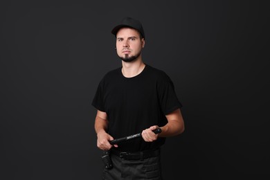 Young bodyguard with baton on black background