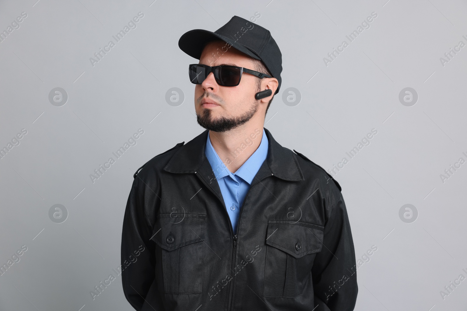 Photo of Security guard in uniform and sunglasses on grey background