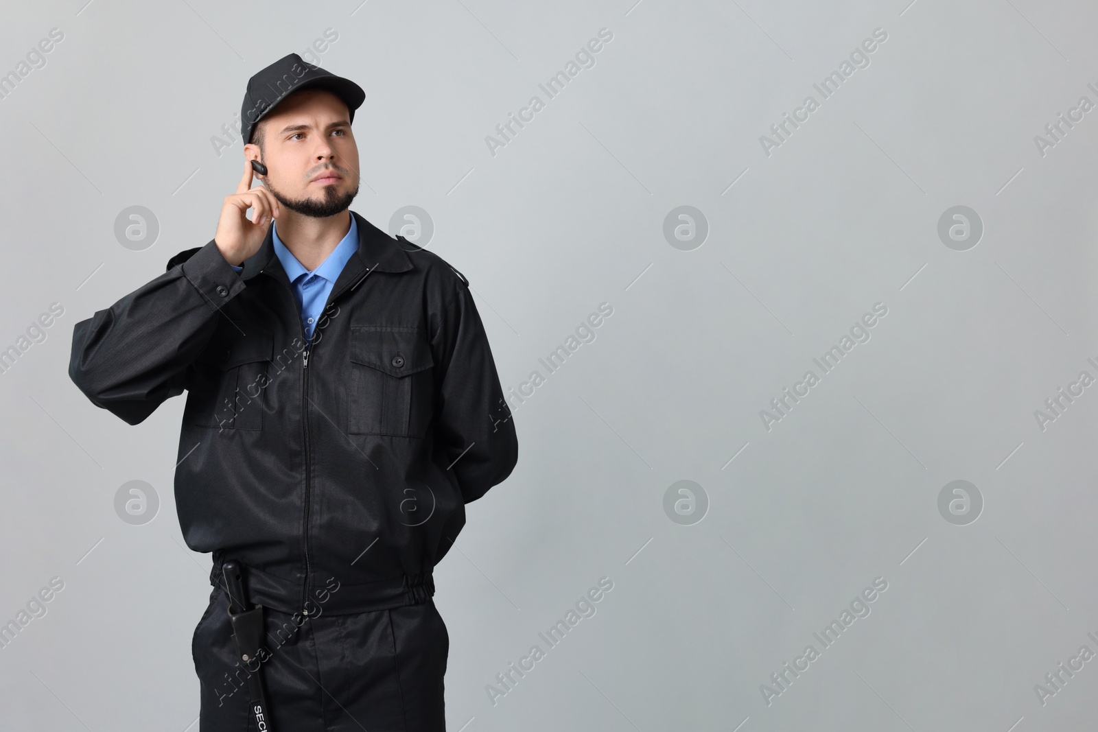 Photo of Security guard in uniform with earpiece on grey background, space for text