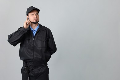 Photo of Security guard in uniform with earpiece on grey background, space for text