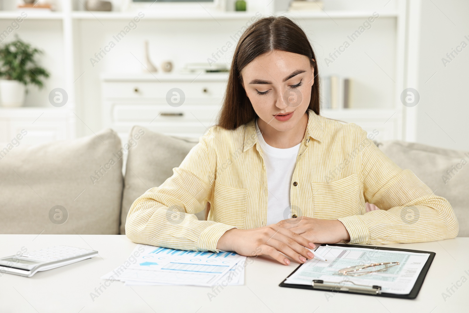 Photo of Budget planning. Beautiful young woman with papers at white table indoors