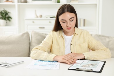 Budget planning. Beautiful young woman with papers at white table indoors