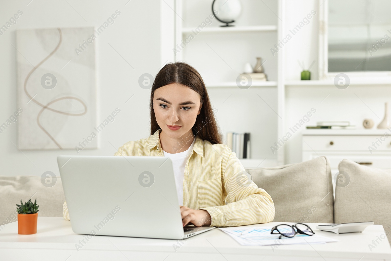 Photo of Budget planning. Young woman with papers using laptop at white table indoors