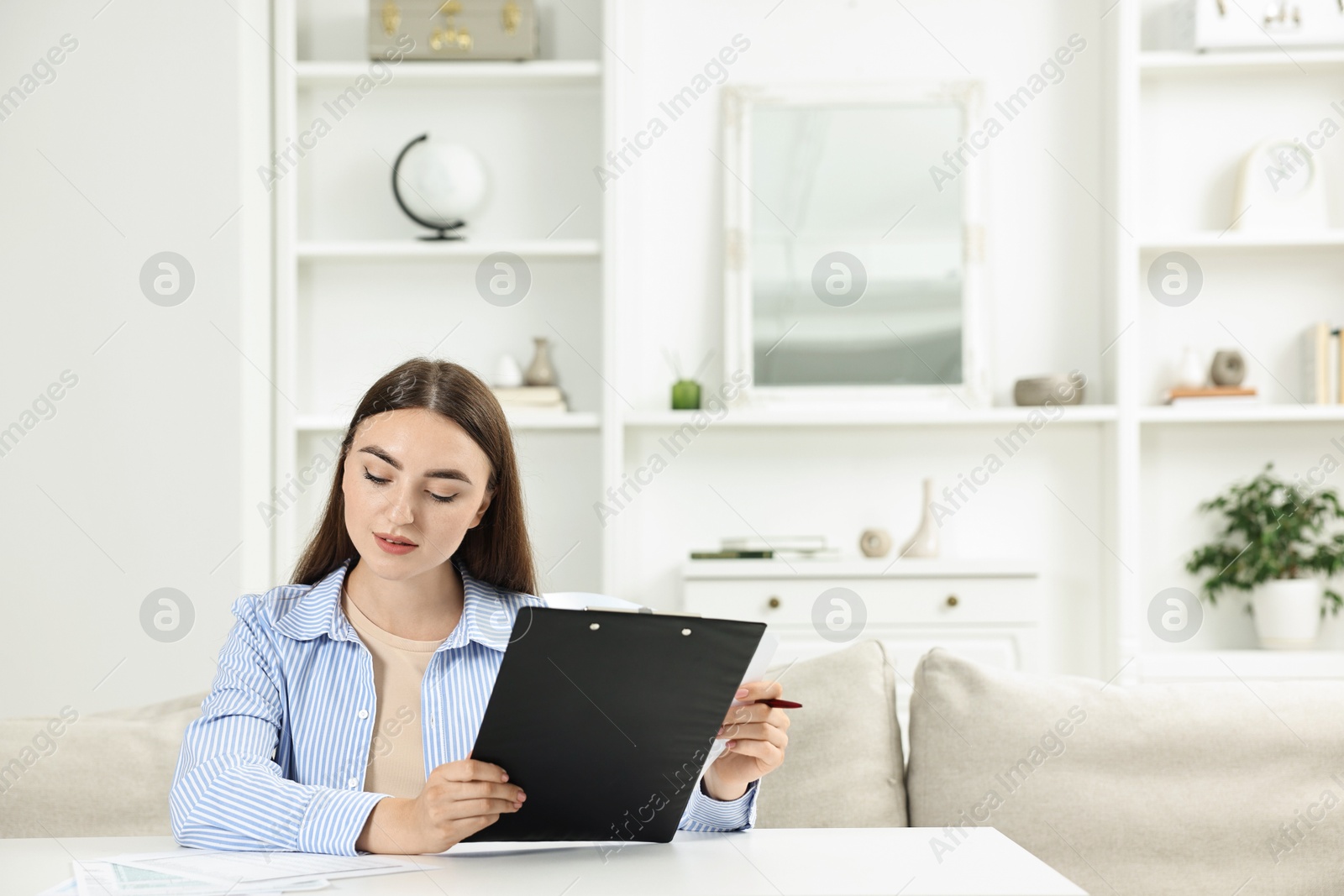 Photo of Budget planning. Beautiful young woman with papers at white table indoors