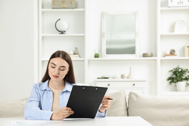 Photo of Budget planning. Beautiful young woman with papers at white table indoors