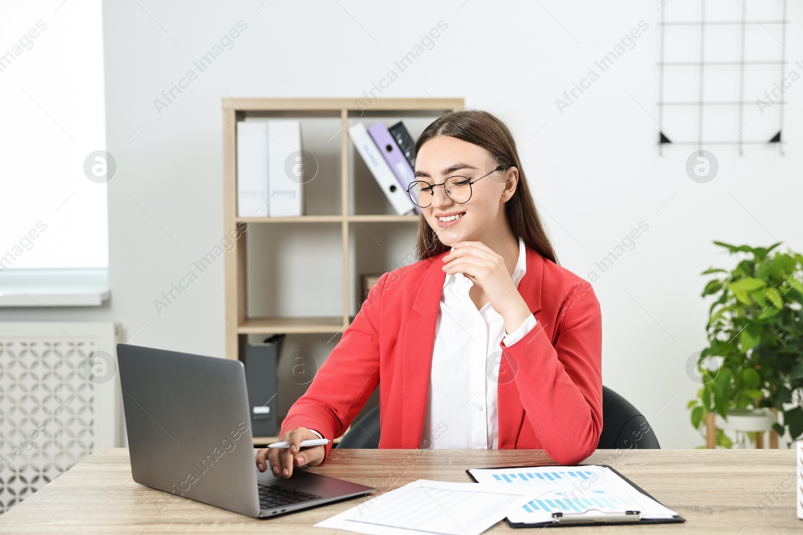 Photo of Budget planning. Young woman with papers using laptop at wooden table in office