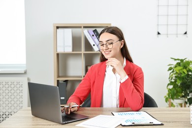 Budget planning. Young woman with papers using laptop at wooden table in office