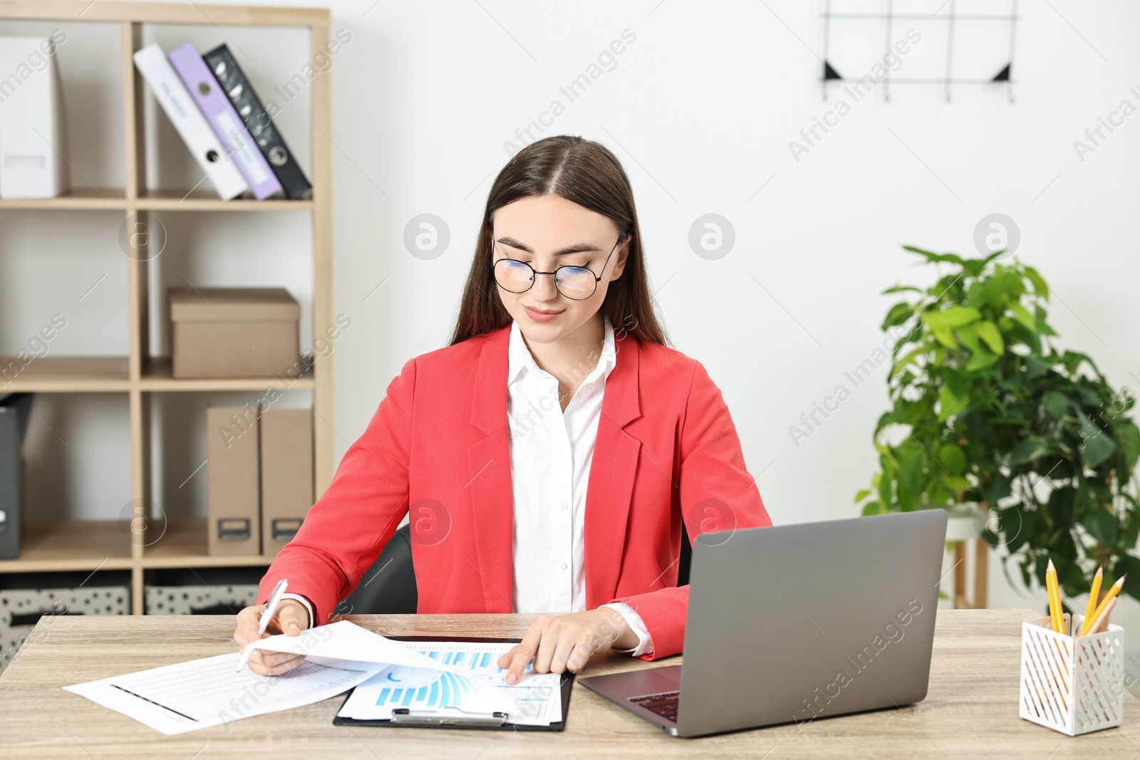 Photo of Budget planning. Young woman with papers and laptop at wooden table in office