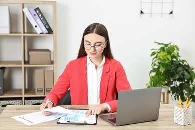 Budget planning. Young woman with papers and laptop at wooden table in office