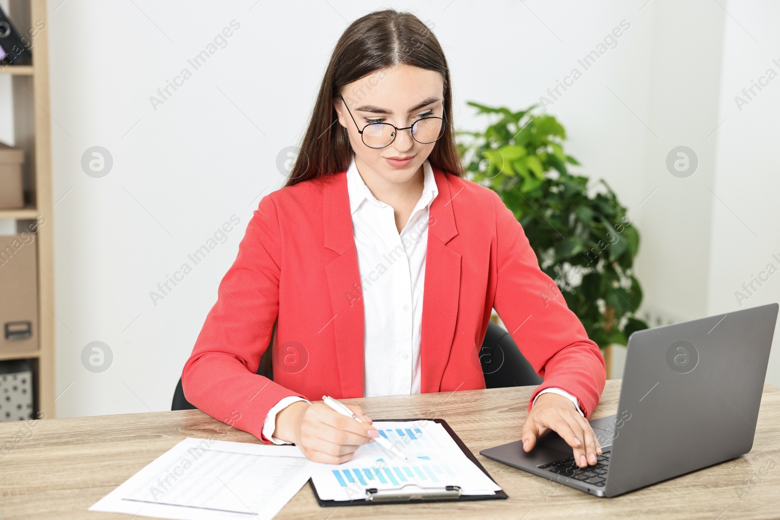 Photo of Budget planning. Young woman with papers using laptop at wooden table in office