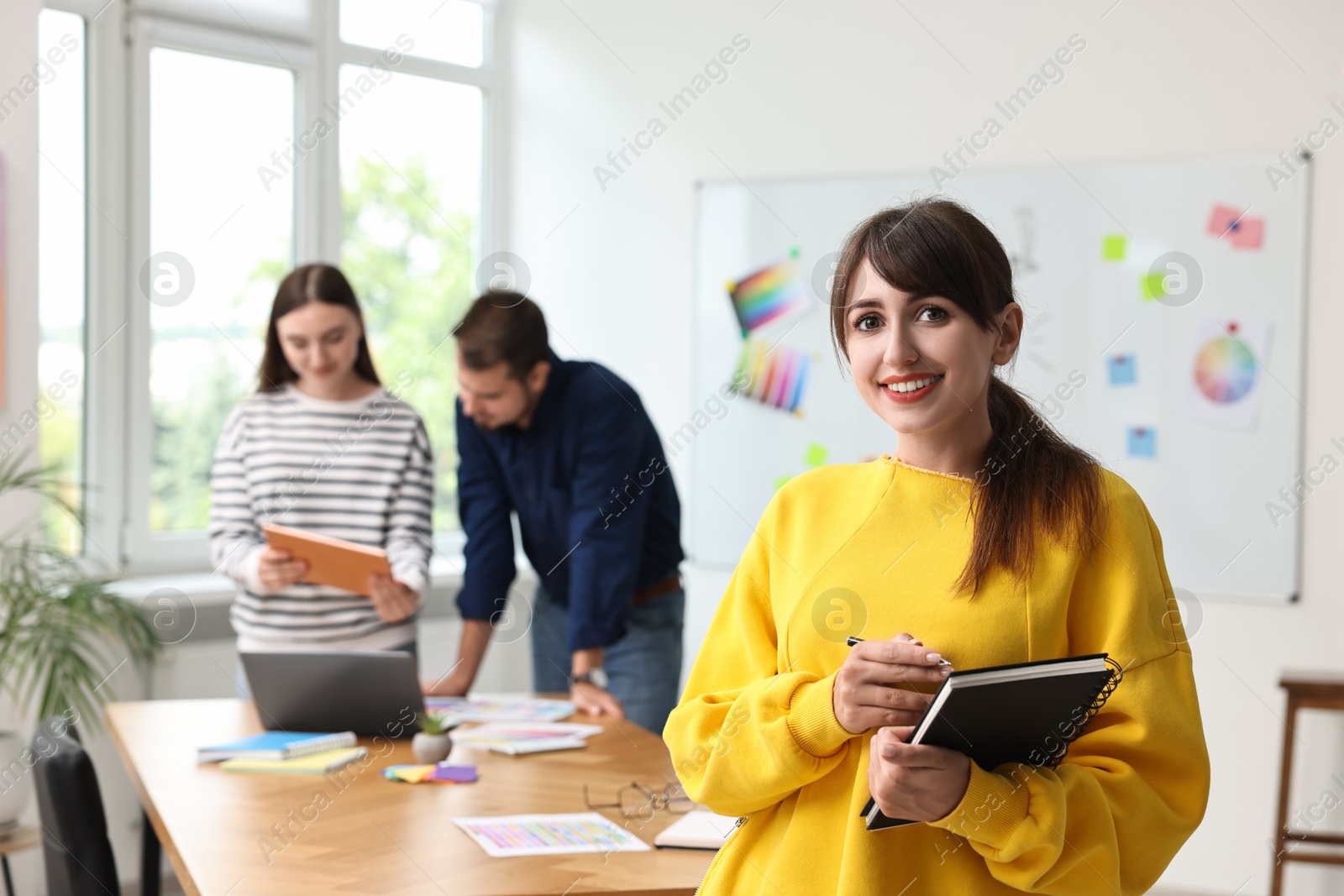 Photo of Portrait of happy young designer with notebook in office