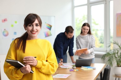 Portrait of happy young designer with notebook in office