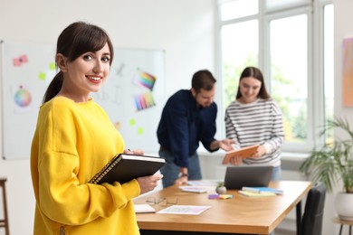 Photo of Portrait of happy young designer with notebook in office