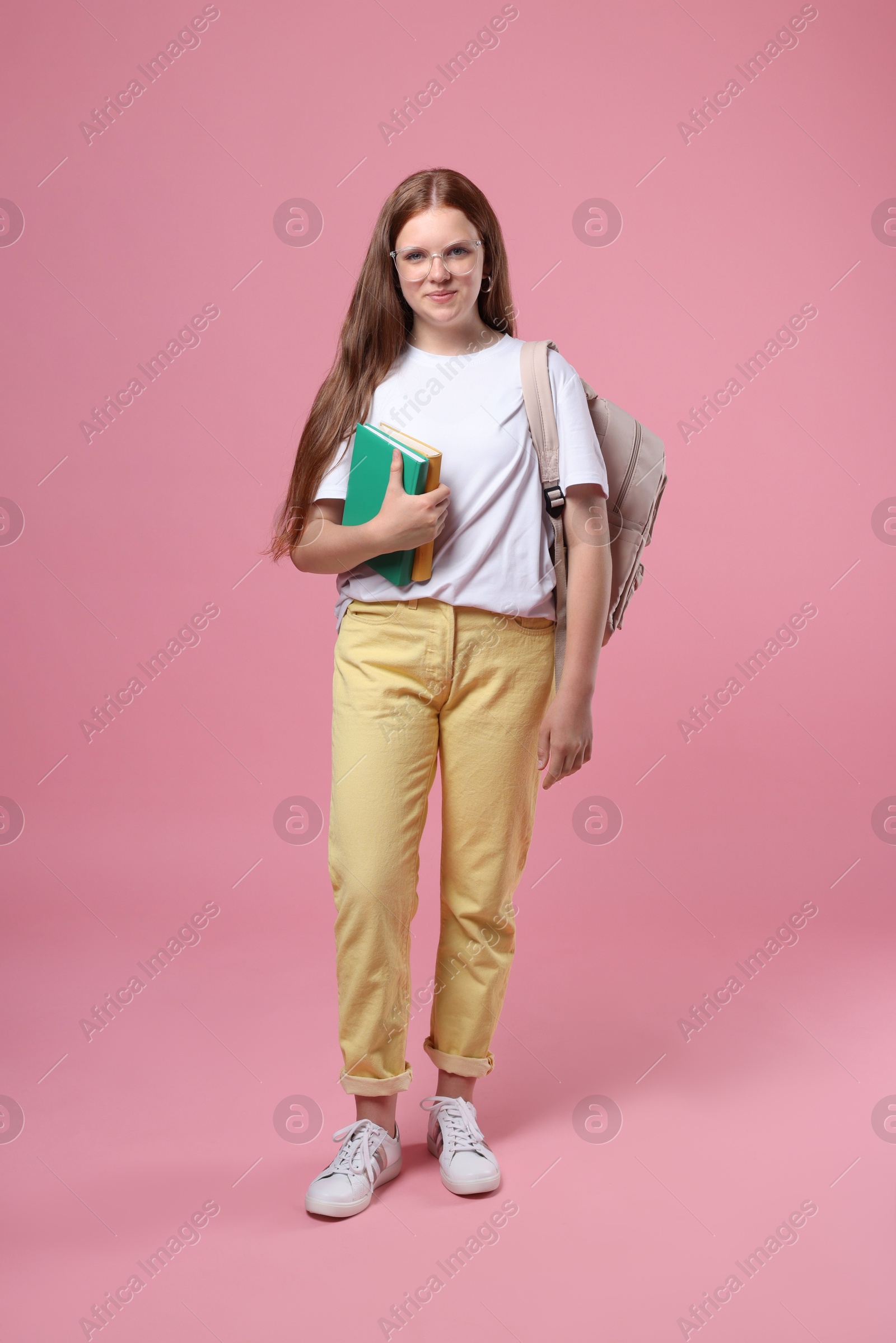 Photo of Teenage girl with backpack and books on pink background