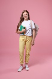 Teenage girl with backpack and books on pink background