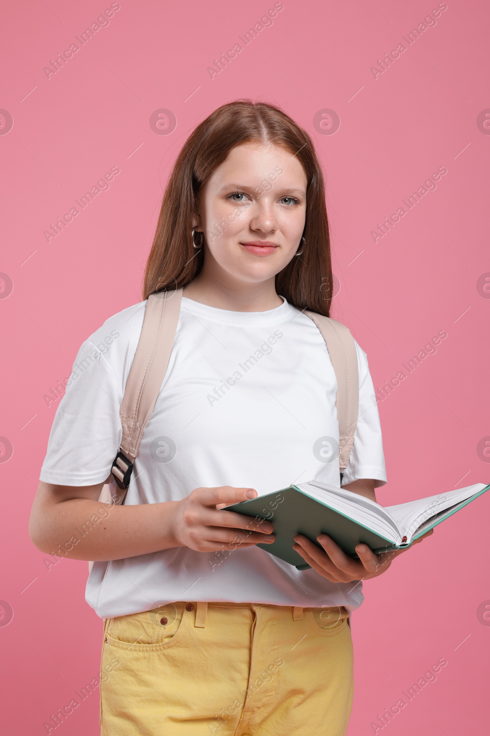 Photo of Teenage girl with backpack and open book on pink background