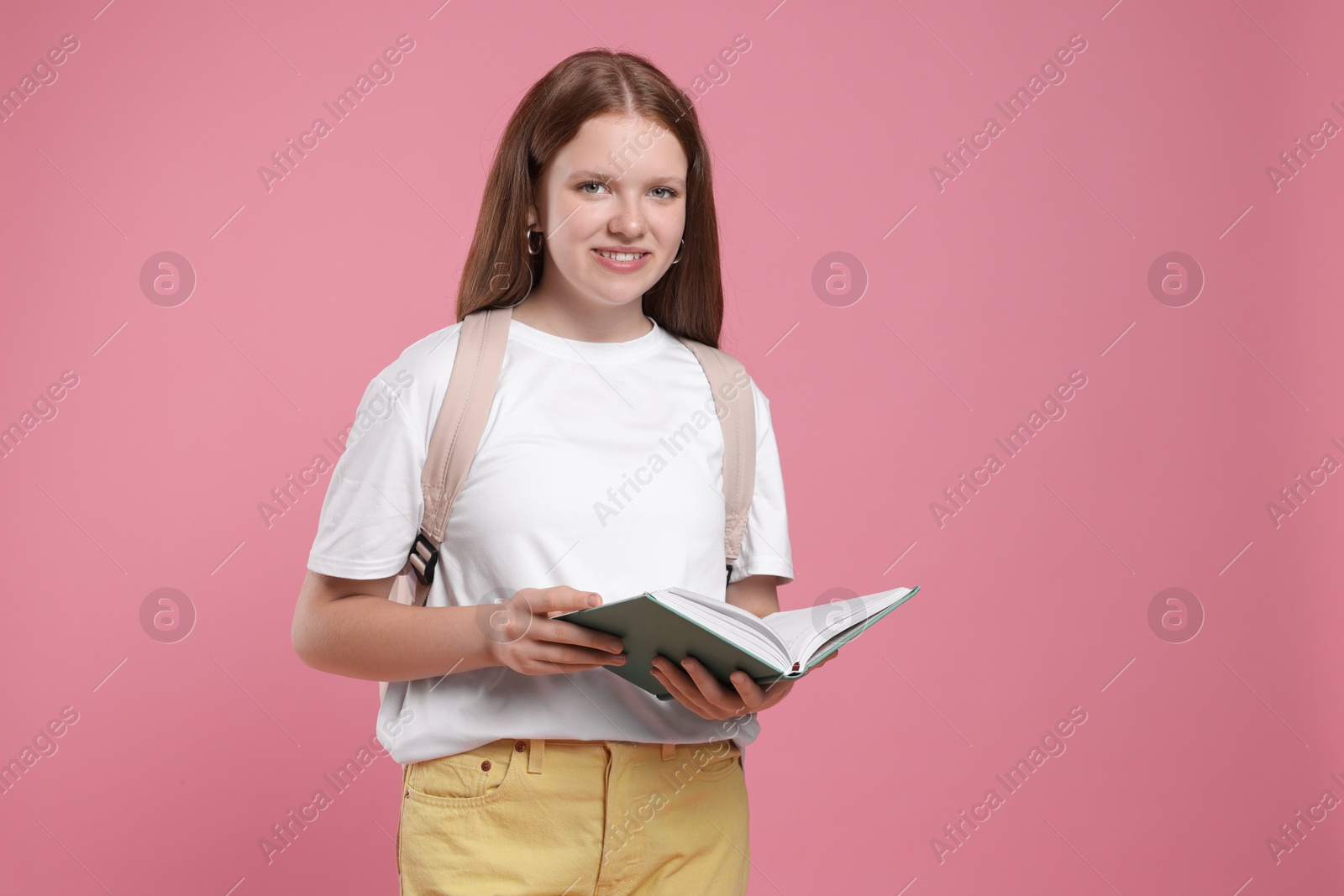 Photo of Teenage girl with backpack and open book on pink background