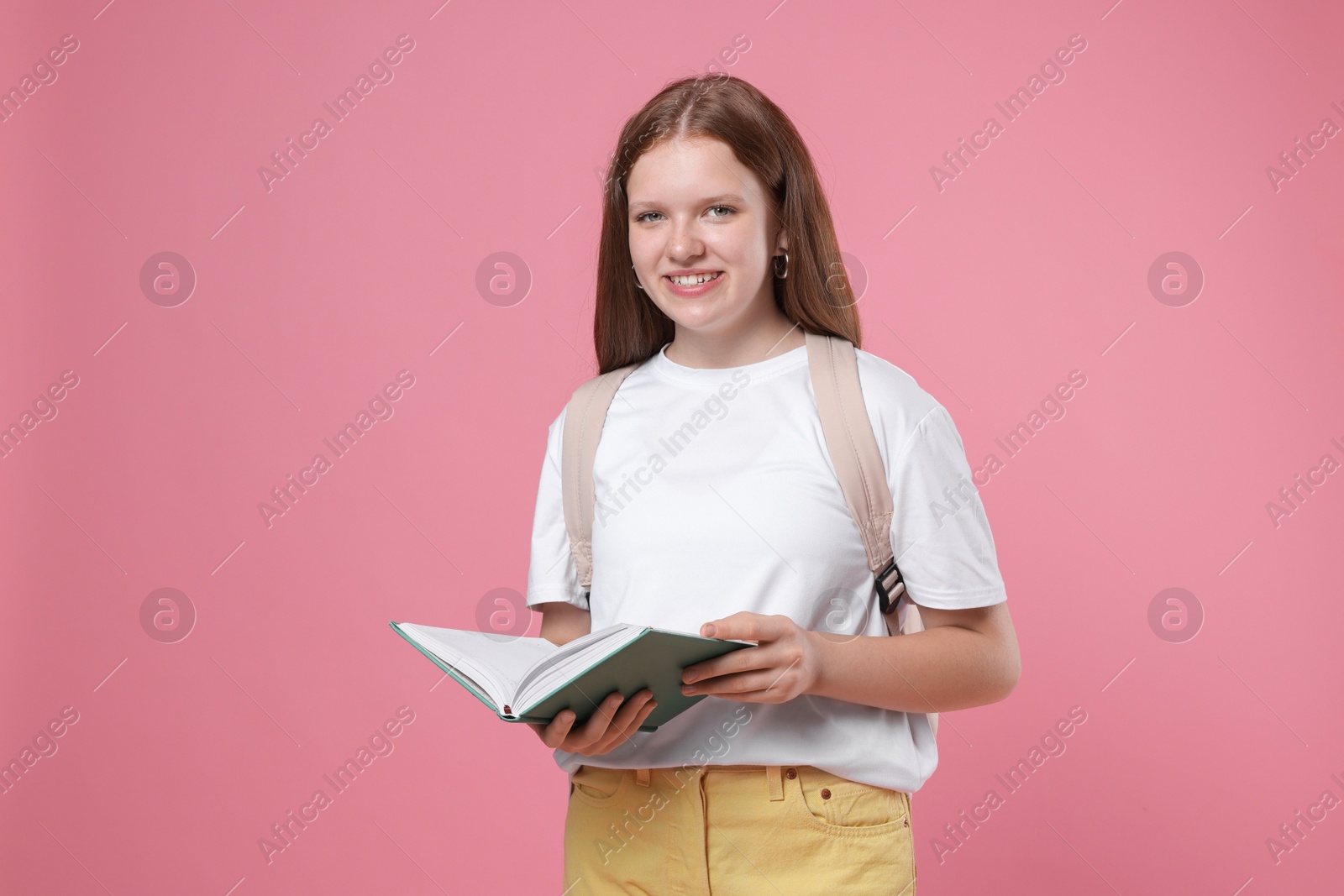 Photo of Teenage girl with backpack and open book on pink background