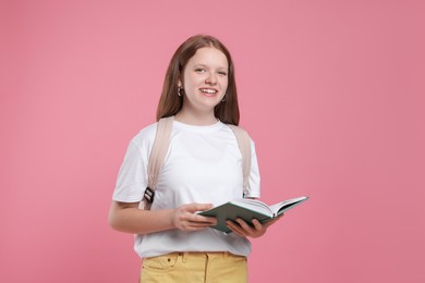 Teenage girl with backpack and open book on pink background