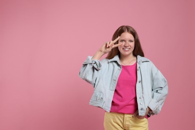 Teenage girl with showing v-sign on pink background, space for text