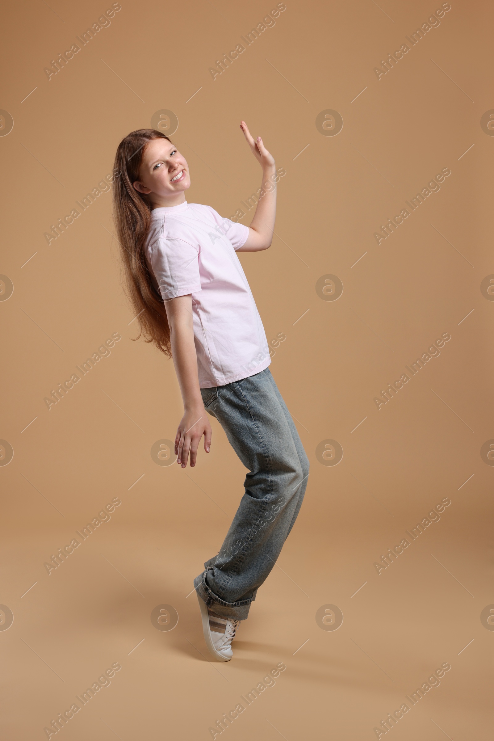 Photo of Cheerful teenage girl dancing on beige background