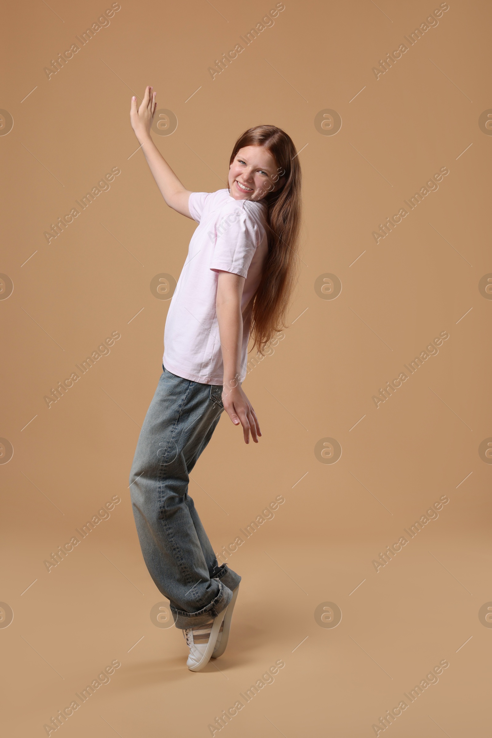 Photo of Cheerful teenage girl dancing on beige background