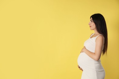 Portrait of beautiful pregnant woman on yellow background, space for text