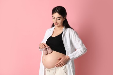 Photo of Portrait of beautiful pregnant woman with baby shoes on pink background