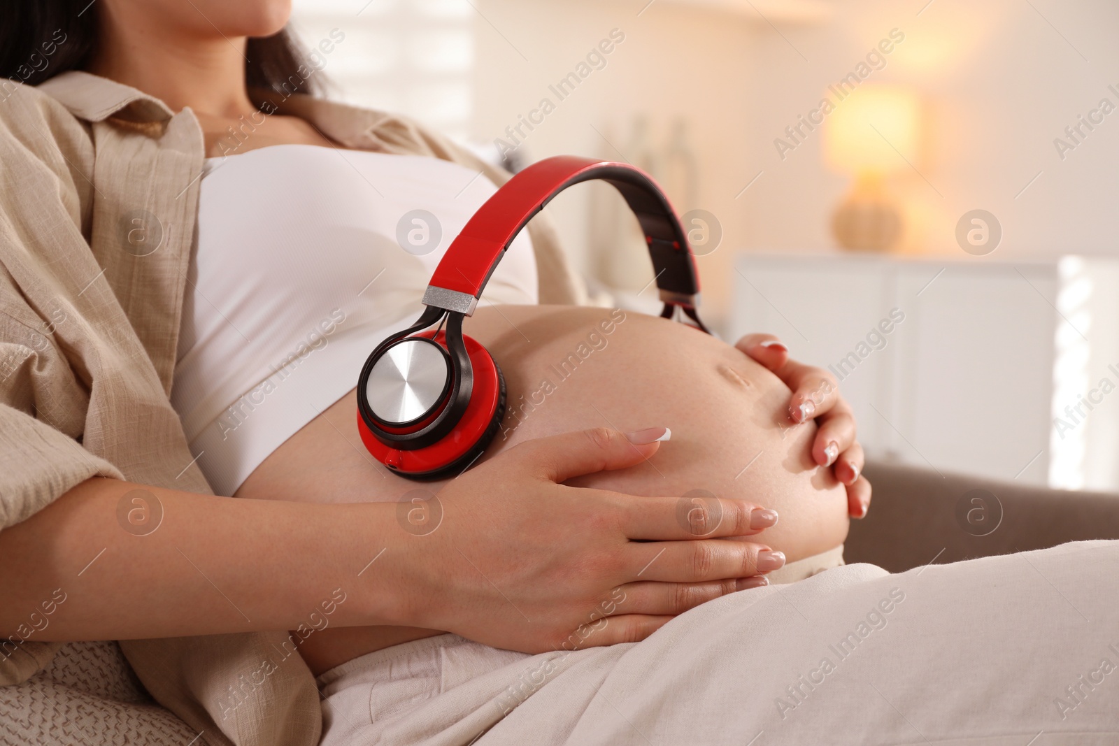 Photo of Young pregnant woman with headphones on belly at home, closeup