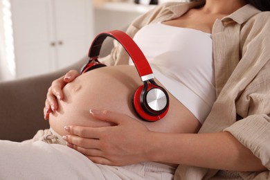 Photo of Young pregnant woman with headphones on belly at home, closeup