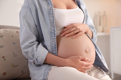 Photo of Young pregnant woman sitting on sofa at home, closeup