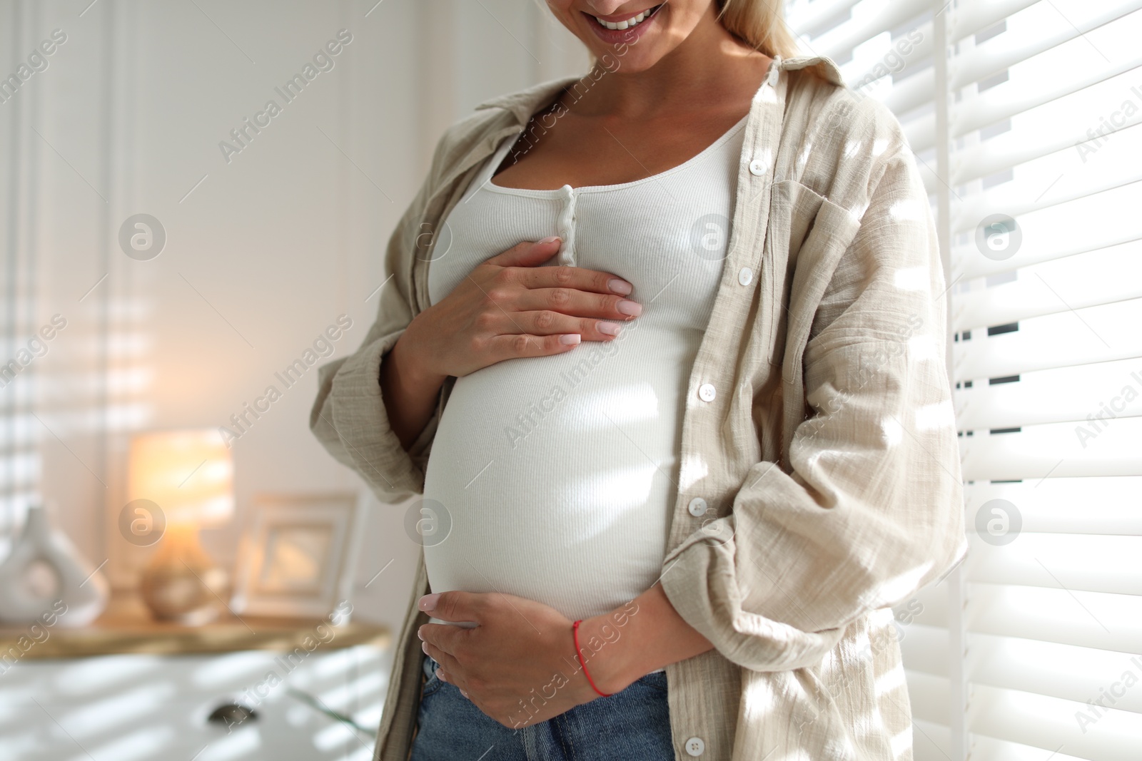 Photo of Pregnant woman near window at home, closeup