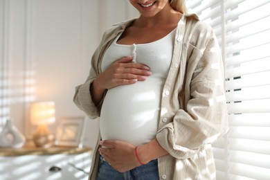 Photo of Pregnant woman near window at home, closeup