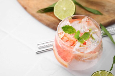 Photo of Refreshing water with grapefruit and mint in glass on white tiled table, closeup. pace for text