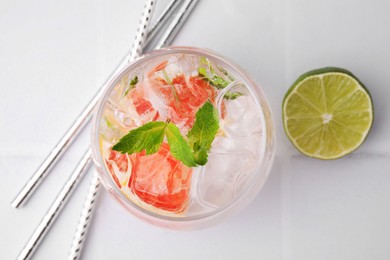 Photo of Refreshing water with grapefruit and mint in glass on white tiled table, flat lay