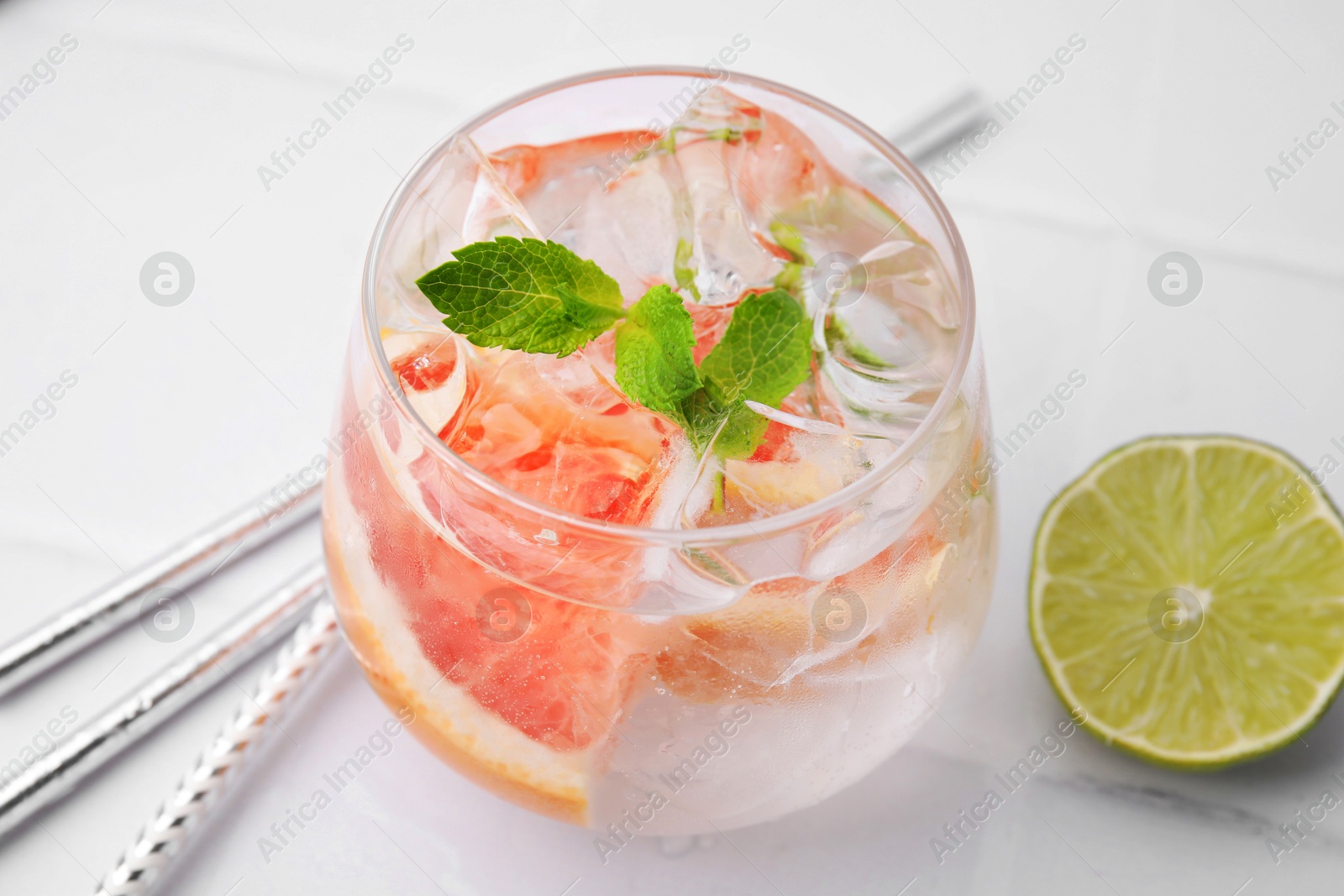 Photo of Refreshing water with grapefruit and mint in glass on white tiled table, closeup