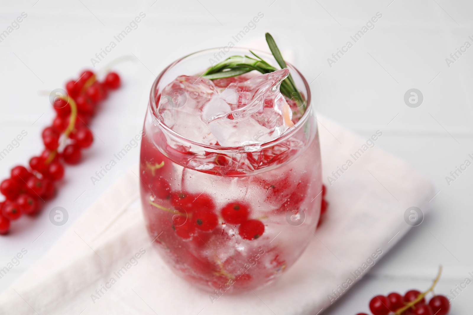 Photo of Refreshing water with red currants and rosemary in glass on white table, closeup